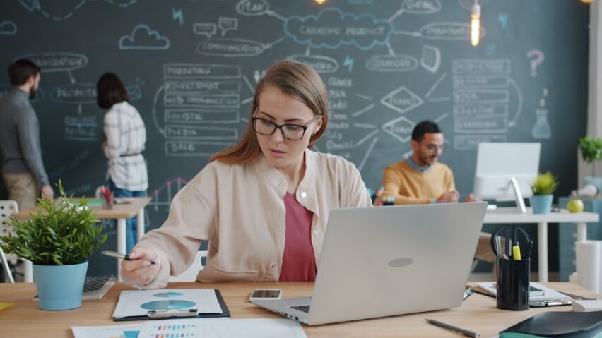 Person with a concerned expression sits at a modern desk, reviewing financial documents and a calculator, representing the...