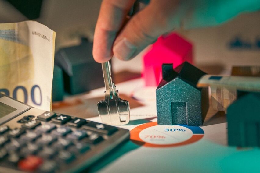 Close-up shot of a hand discreetly pulling cash out of a piggy bank shaped like a house, symbolizing hidden real estate fees.