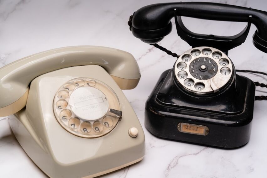 Vintage rotary telephone sits next to a sleek, modern smartphone on a clean surface, symbolizing technological evolution a...