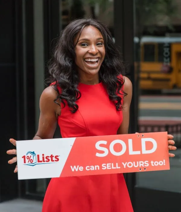 A 1 Percent Lists client holding a Sold sign outside their home