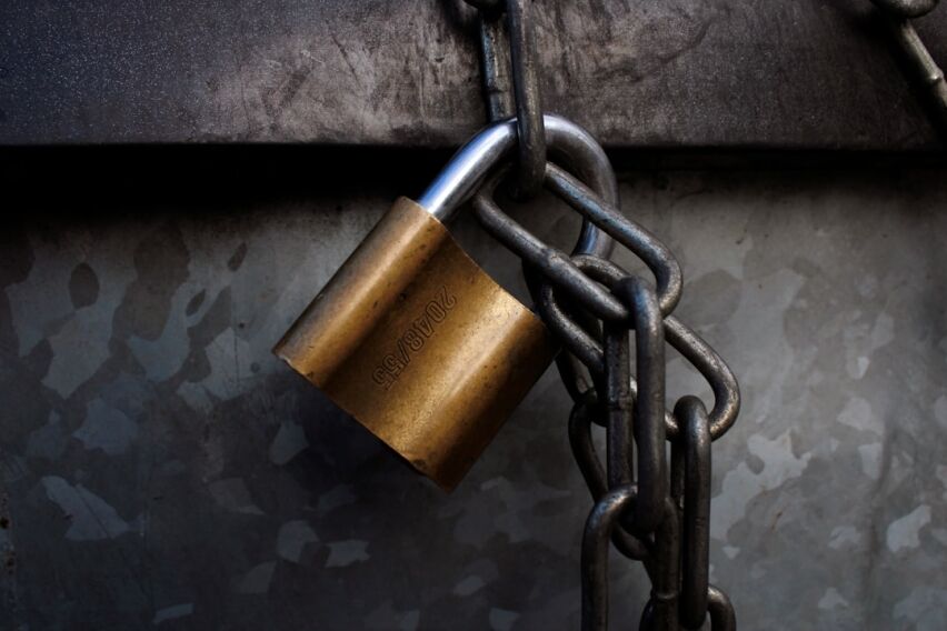 Minimalist photo of a small model house wrapped in a heavy chain and secured with a padlock, representing the financial bu...