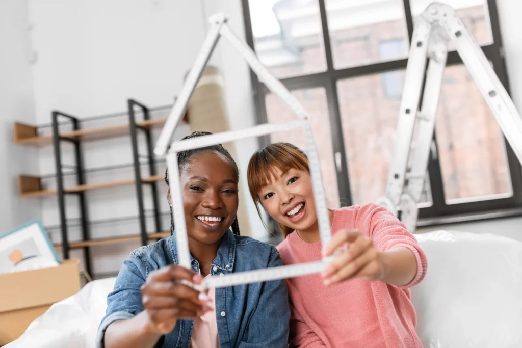 Moving people and real estate concept happy smiling women with ruler folded in shape of house at new home happy smiling wo...