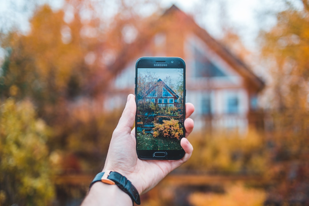 A person holds a smartphone displaying a real estate app while standing inside a bright, modern home, illustrating the convenience and transparency of technology in property transactions.