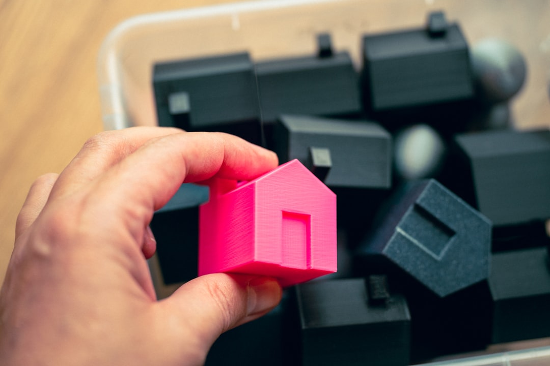 A person's hand carefully places a coin into a white, house-shaped piggy bank, representing the concept of saving money on real estate commissions.
