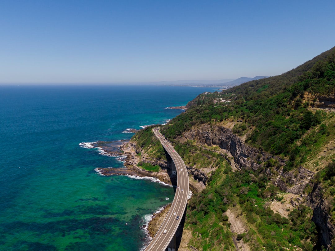 A single car driving along a dangerous cliffside road, symbolizing the perilous and collapsing 6% real estate commission model.