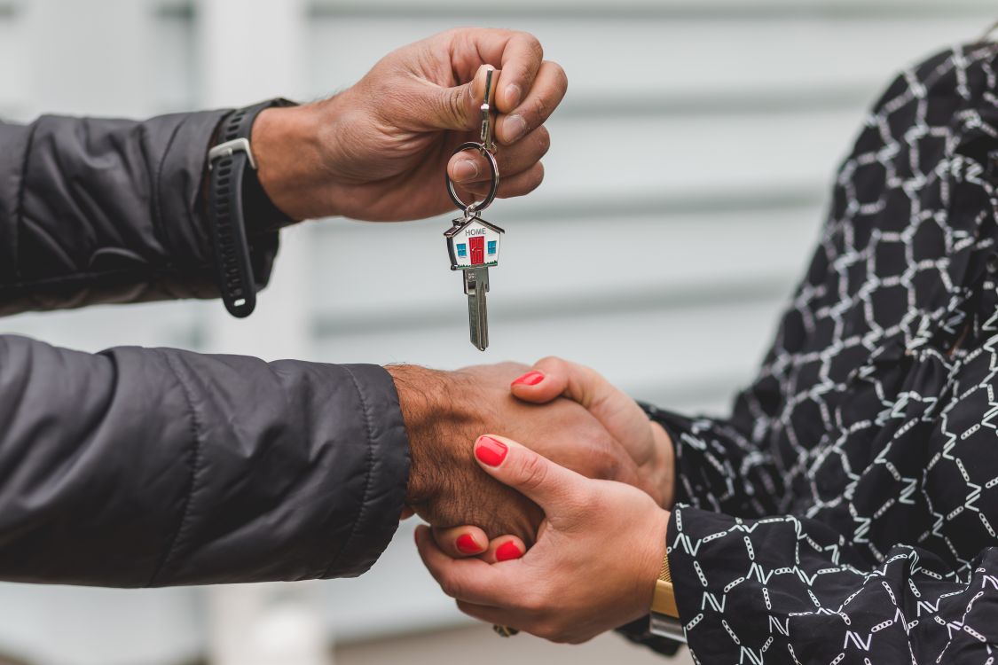 A well-dressed, confident person sitting at a modern table holding a set of house keys, representing a seller in a powerful negotiating position.
