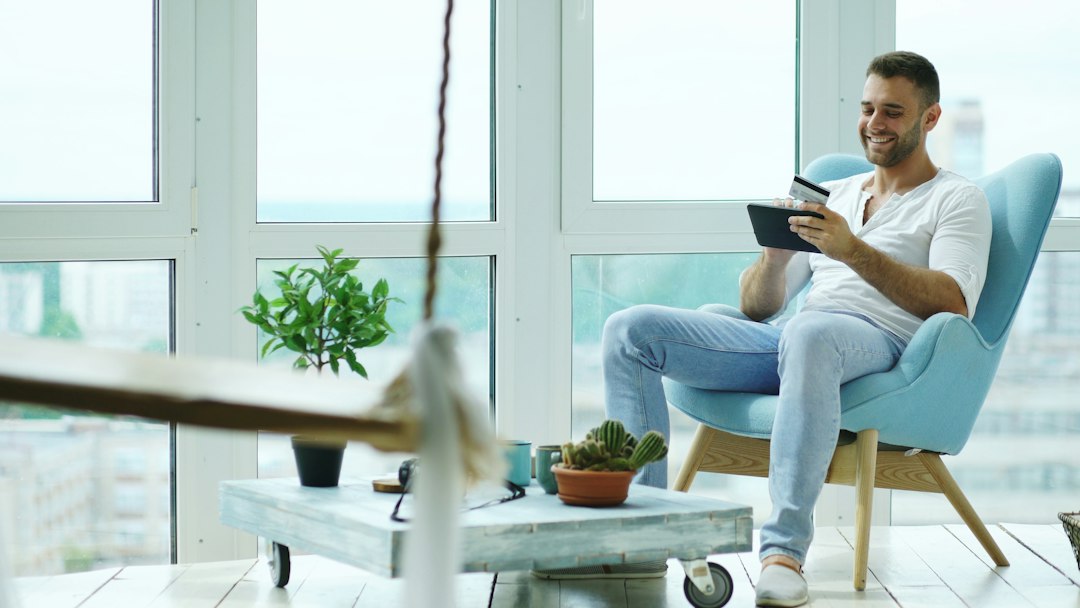 A person comfortably uses a tablet to view property details inside a bright, minimalist, and modern home, showcasing the ease of digital real estate.