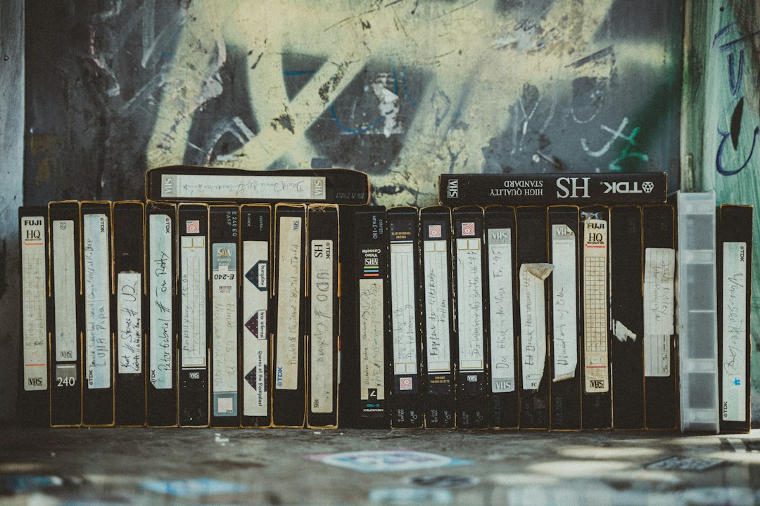 Stack of dusty, obsolete VHS tapes sits next to a sleek, modern laptop, symbolizing the transition from outdated to curren...