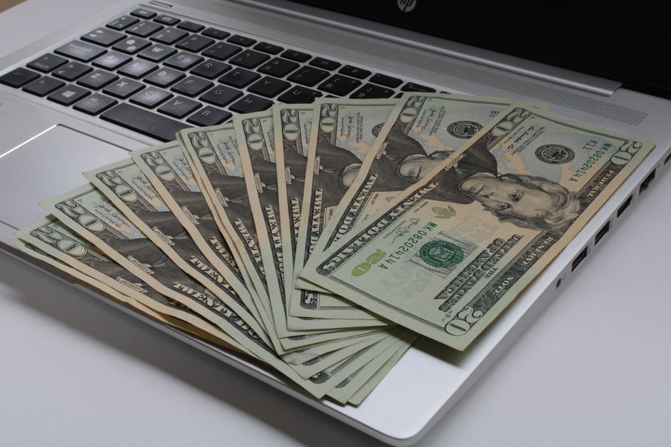 A modern desk with a stack of cash sitting next to an open laptop, representing the financial dividend generated by technology in real estate.