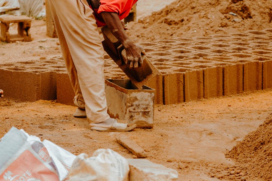 A person's hand carefully removing a block from a small house built from wooden blocks, symbolizing the unbundling of traditional real estate agent tasks.