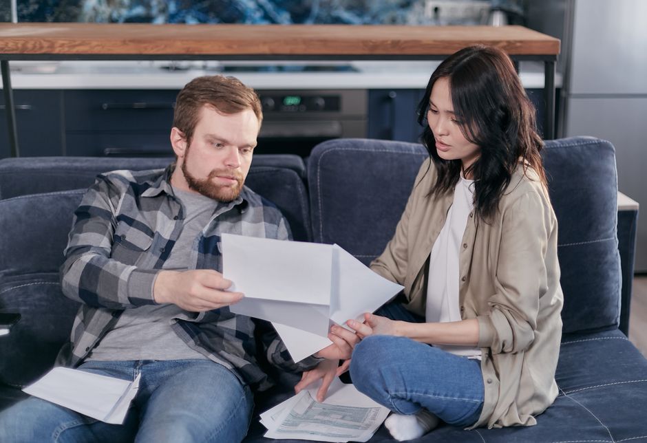 A professional couple sits in a bright, modern living room, smiling as they review financial papers, conveying a sense of relief and success in managing their home's equity.