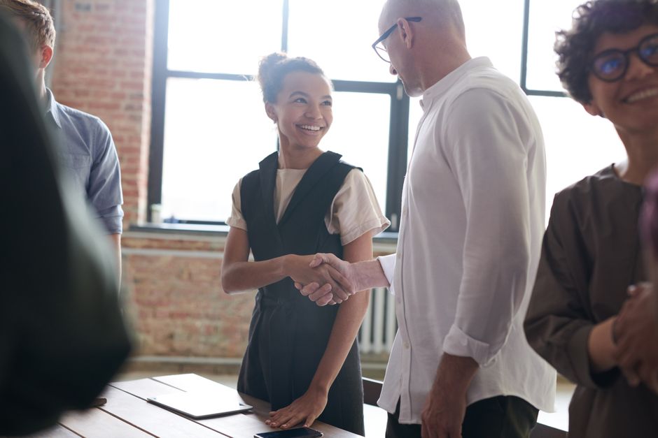 Two professionals shaking hands in the living room of a modern, brightly lit home, signifying a successful real estate negotiation and deal.