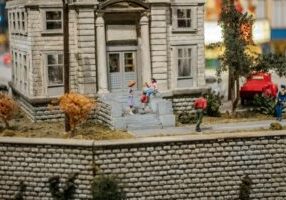Close-up, professional shot of a person using a magnifying glass to scrutinize a small model of a house, symbolizing a clo...