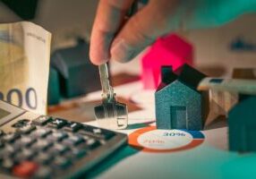 Close-up shot of a hand discreetly pulling cash out of a piggy bank shaped like a house, symbolizing hidden real estate fees.
