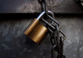 Minimalist photo of a small model house wrapped in a heavy chain and secured with a padlock, representing the financial bu...