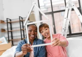 Moving people and real estate concept happy smiling women with ruler folded in shape of house at new home happy smiling wo...