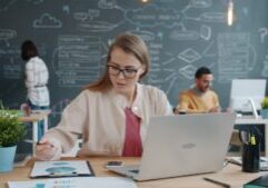 Person with a concerned expression sits at a modern desk, reviewing financial documents and a calculator, representing the...