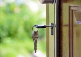 Person's hand gently squeezing a small white model of a house against a clean, bright background, symbolizing the financia...