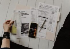 Professionally dressed person sits at a clean, modern desk, looking at a calculator with a stressed or concerned expressio...
