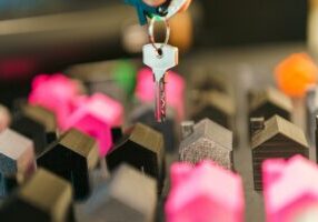 Sharply dressed professional in a modern office carefully analyzes a miniature model of a house, symbolizing a strategic, ...