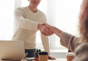 Smiling real estate agent hands a set of house keys to a new homeowner in front of a beautiful modern home, symbolizing a ...
