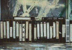 Stack of dusty, obsolete VHS tapes sits next to a sleek, modern laptop, symbolizing the transition from outdated to curren...