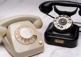 Vintage rotary telephone sits next to a sleek, modern smartphone on a clean surface, symbolizing technological evolution a...